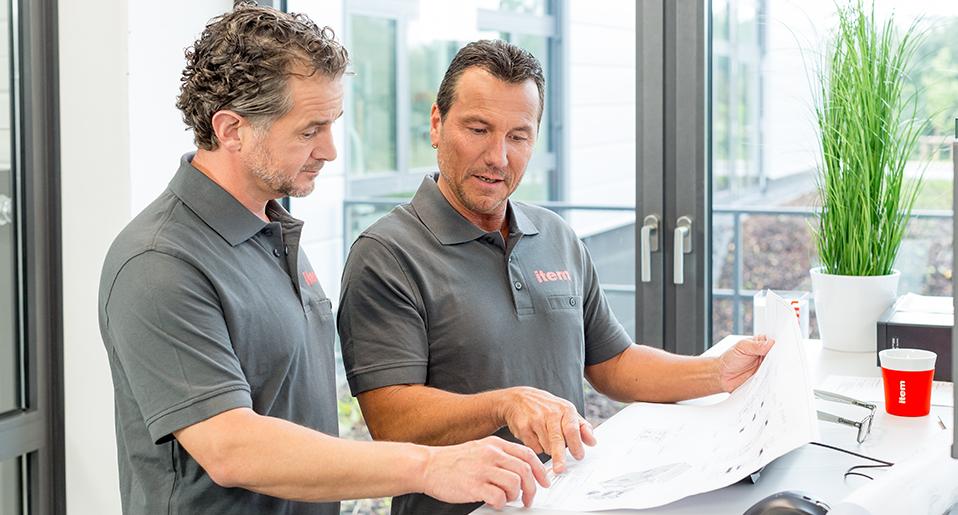 Zwei Mitarbeiter sprechn über Bauzeichnungen, Quelle: item Industrietechnik GmbH Zwei Mitarbeiter sprechn über Bauzeichnungen